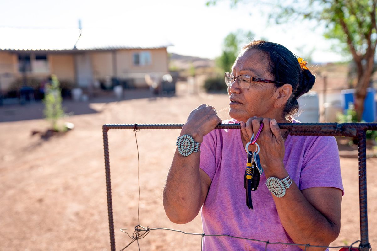 A Navajo woman standing by the gate of her home, with a faraway look in her eyes