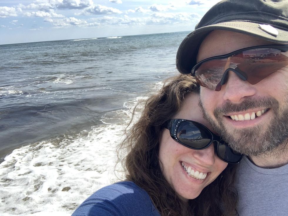 A selfie of Liz and her husband smiling at the camera in front of the ocean