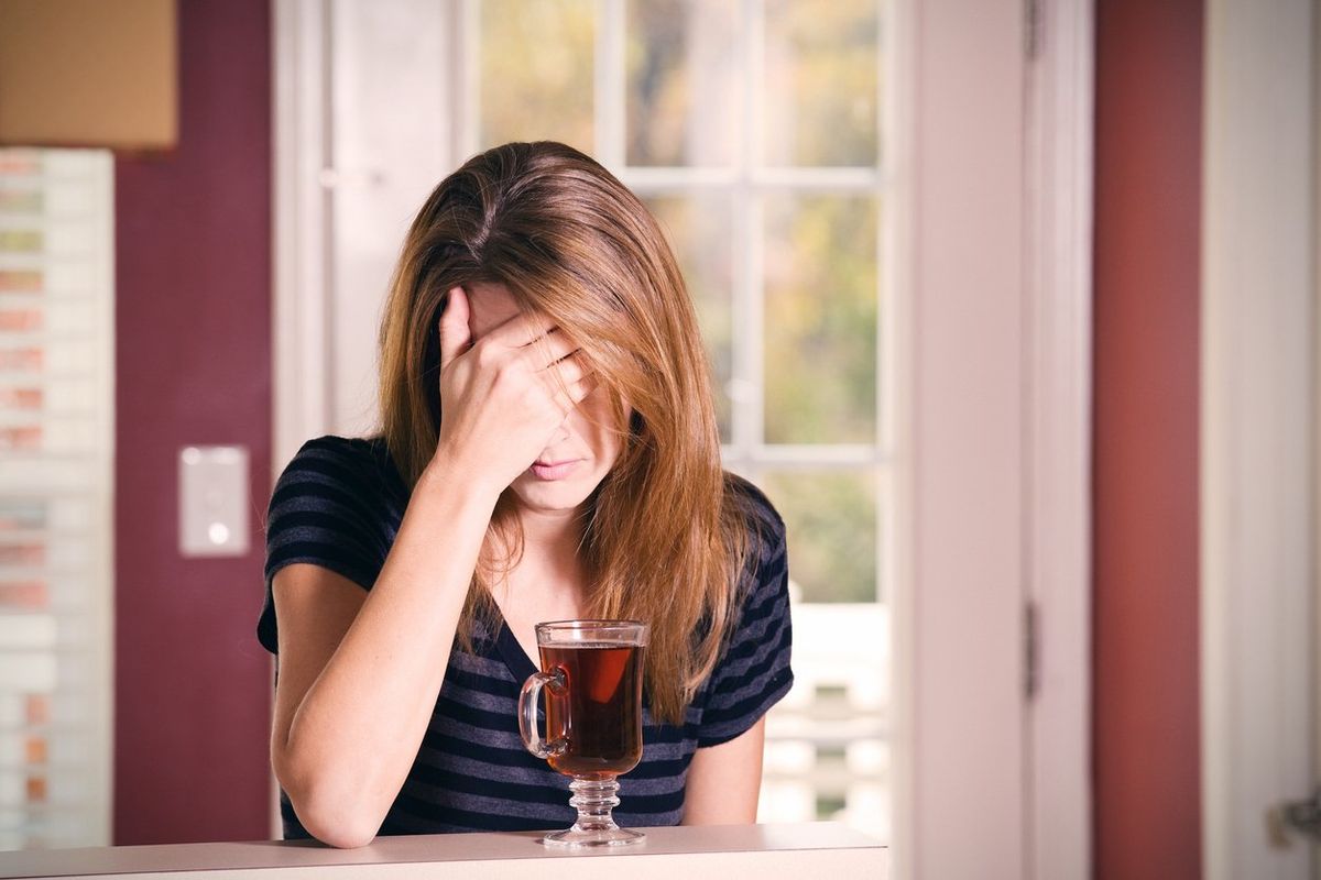 A woman covering her face, dealing with alcohol induced anxiety, drinking tea