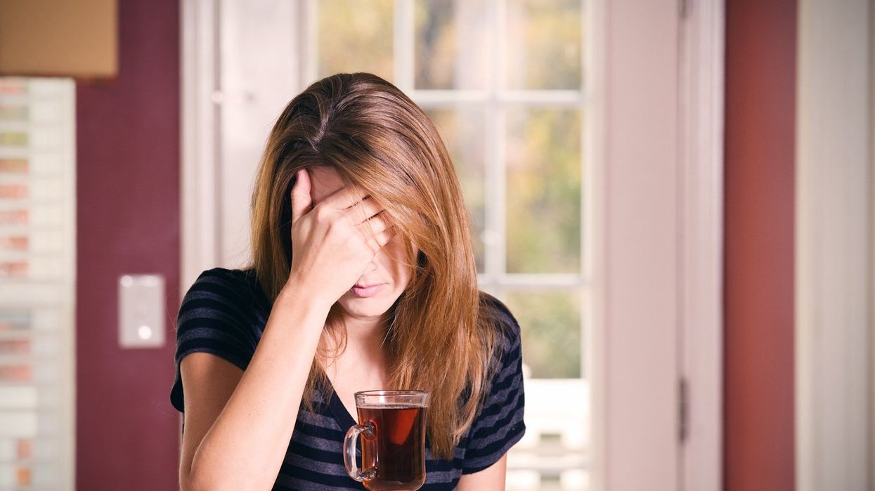 A woman covering her face, dealing with alcohol induced anxiety, drinking tea