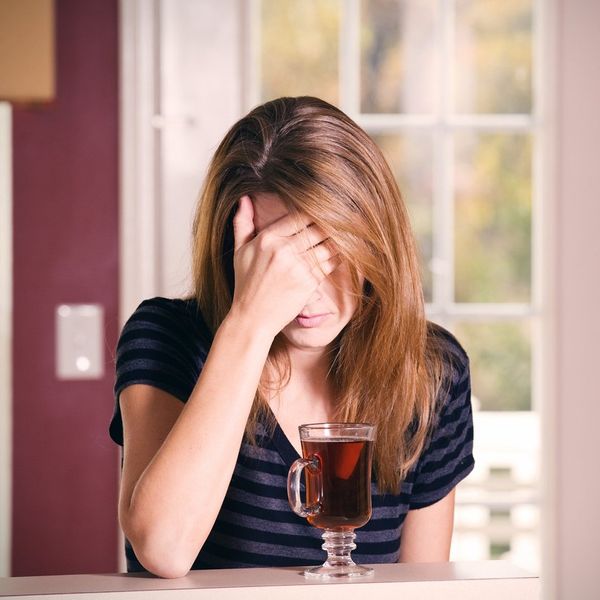 A woman covering her face, dealing with alcohol induced anxiety, drinking tea