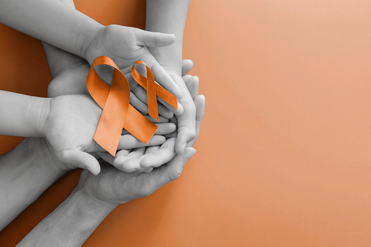 Adult and child hands holding orange Ribbons, Leukemia cancer and Multiple sclerosis awareness