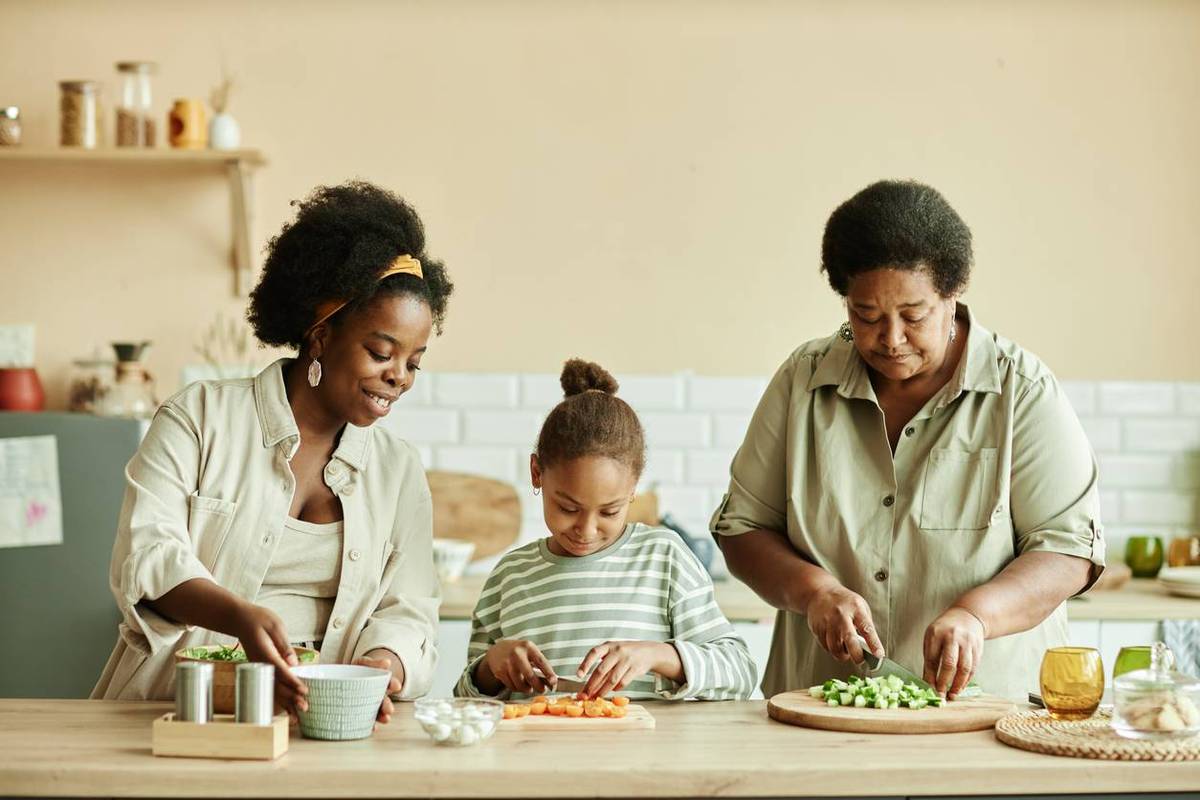 African American family of young smiling mother, daughter and grandmother chopping fresh vegetables