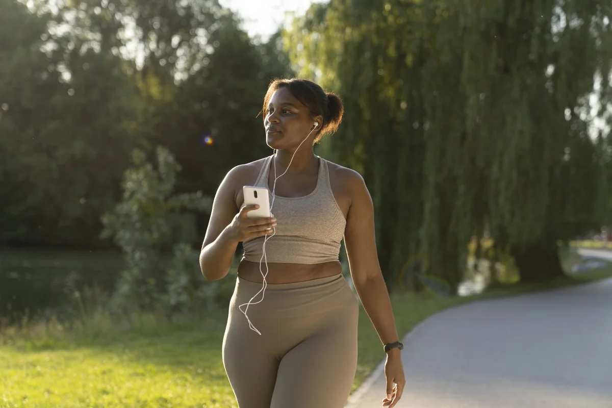 African American woman using mobile phone and earphones during the walking at the park in a summer day