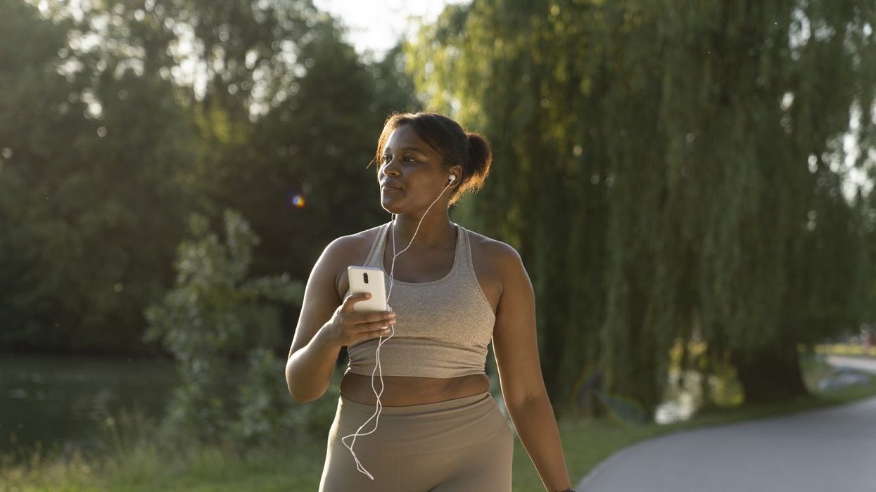 African American woman using mobile phone and earphones during the walking at the park in a summer day