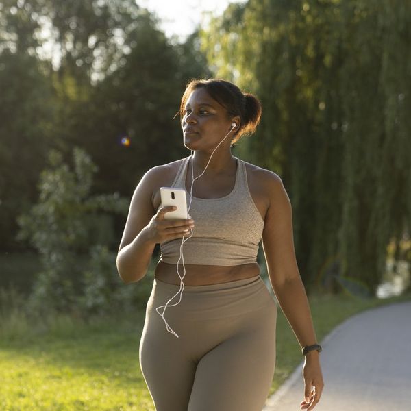 African American woman using mobile phone and earphones during the walking at the park in a summer day