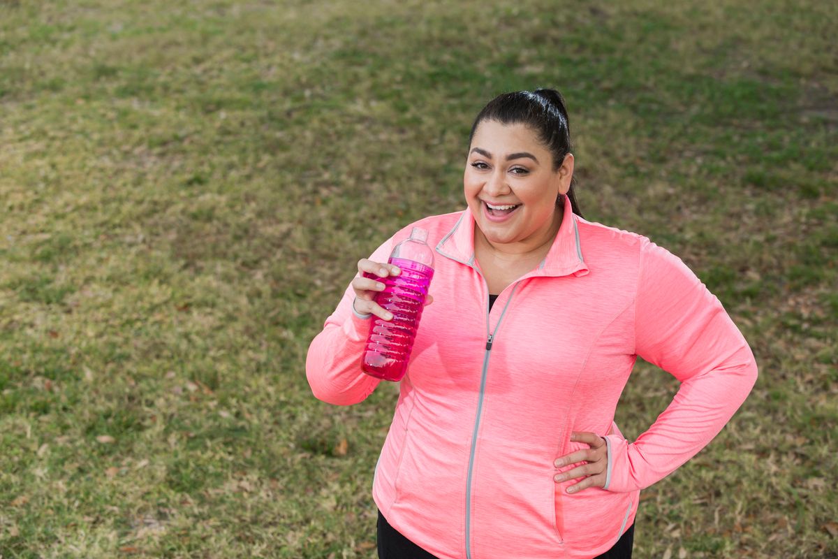 an obese Hispanic woman in her 30s, in the park exercising, taking a break drink water or a sports drink