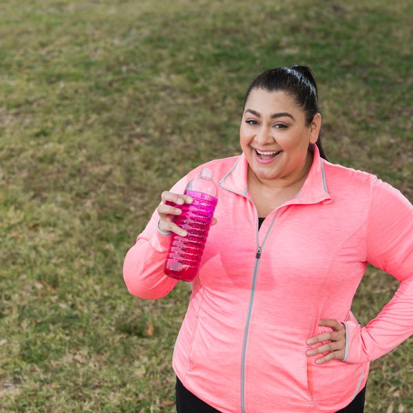 an obese Hispanic woman in her 30s, in the park exercising, taking a break drink water or a sports drink