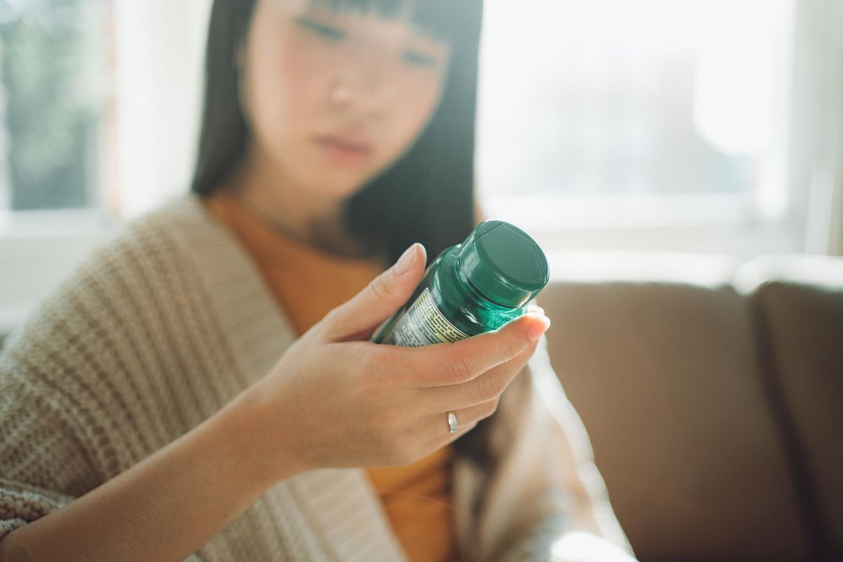 Asian woman looking at label on a bottle of supplements