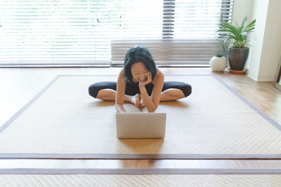 Asian woman practicing yoga at home, she is following an online video class