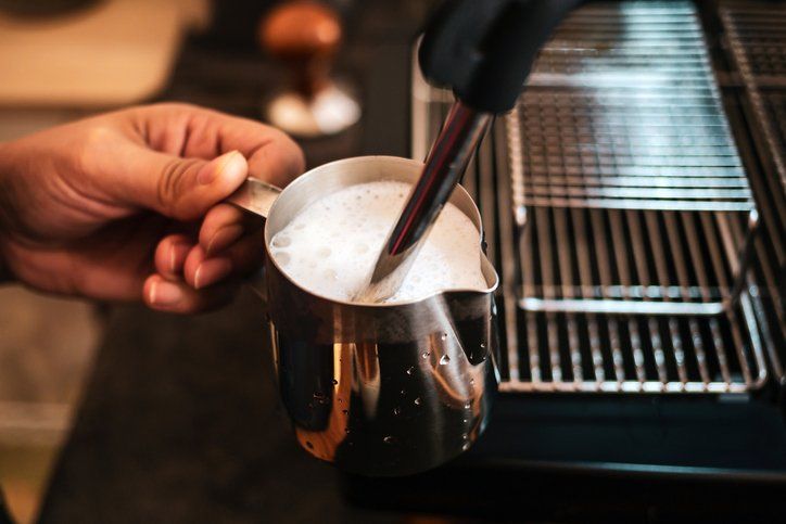 Barista hand using high-pressure steam-operated milk frother