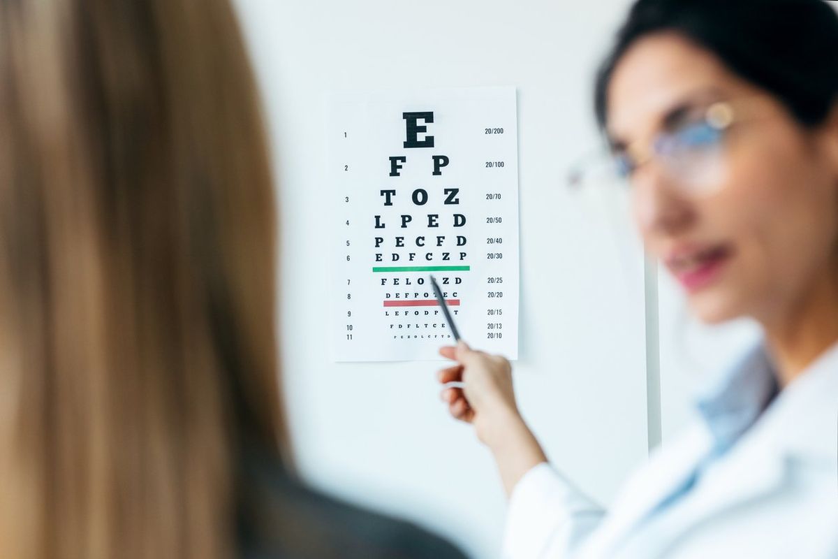 Beautiful female optician doing eye exam with eye chart on her patient in ophthalmology clinic