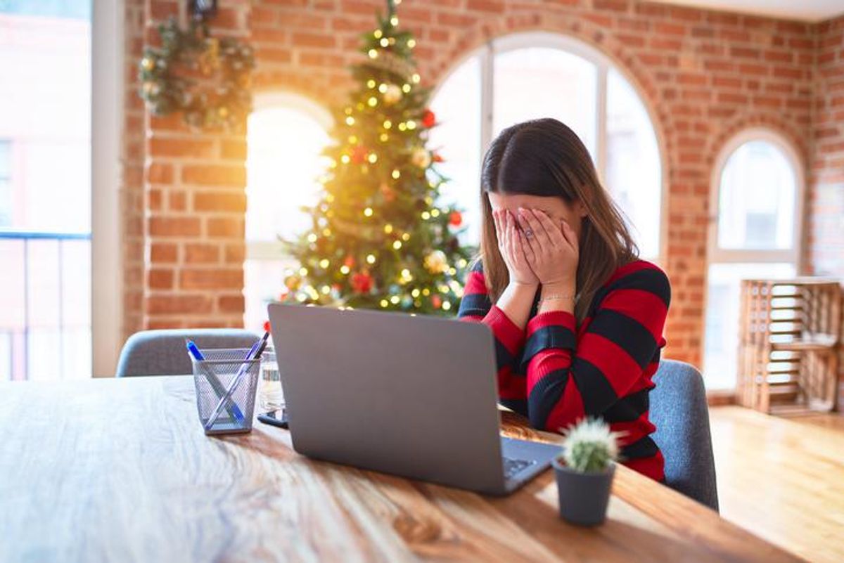 Beautiful woman sitting at the table working with laptop at home around christmas tree with sad expression