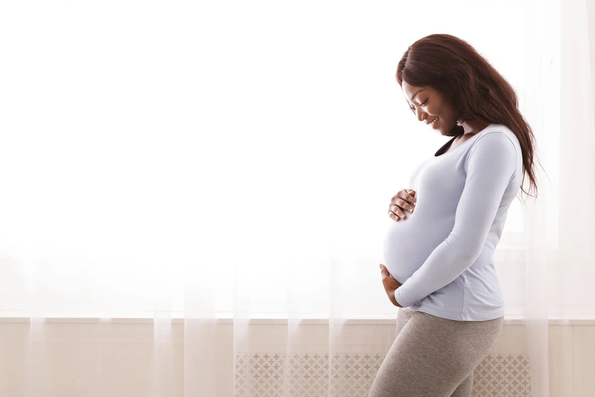 Black pregnant woman hugging her tummy at home