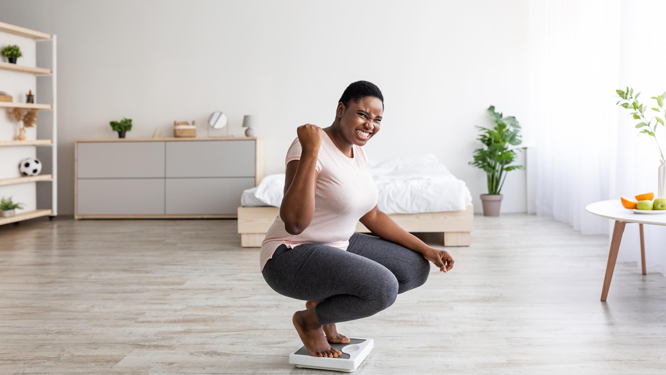 black woman sitting on scales at home, making YES gesture