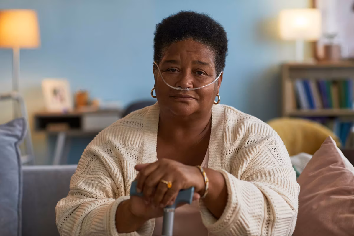 Black woman with copd sitting indoors using oxygen tube