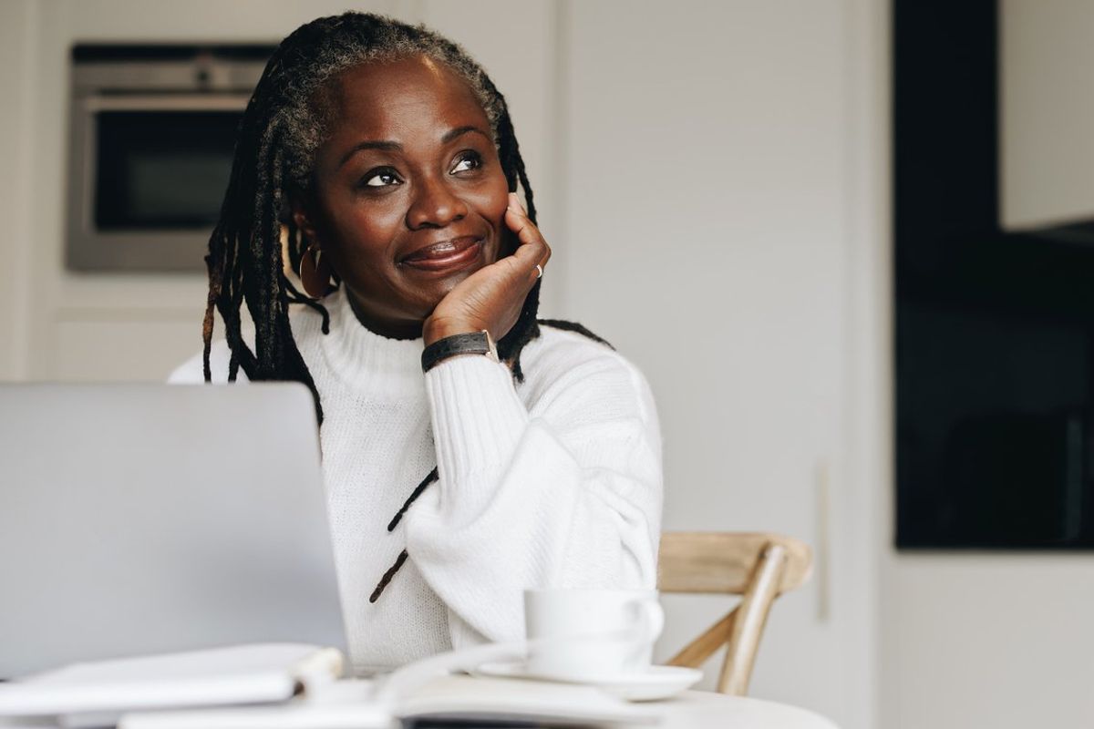 businesswoman looking away thoughtfully while working on a laptop at home
