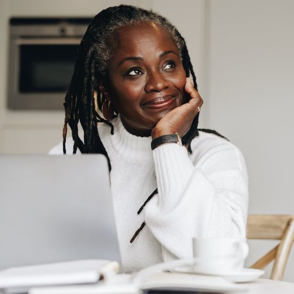 businesswoman looking away thoughtfully while working on a laptop at home