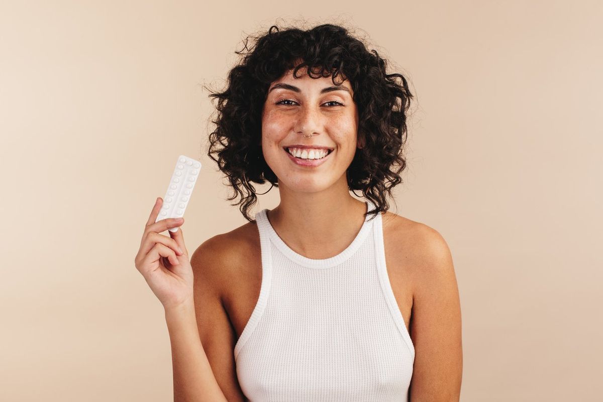 Cheerful young woman smiling at the camera while holding a packet of the progestin-only mini pill
