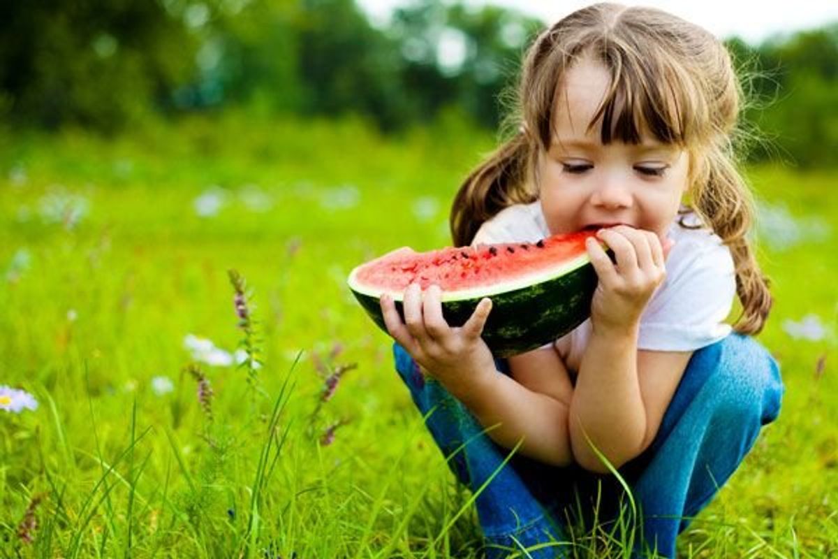 child in a field eating watermelon