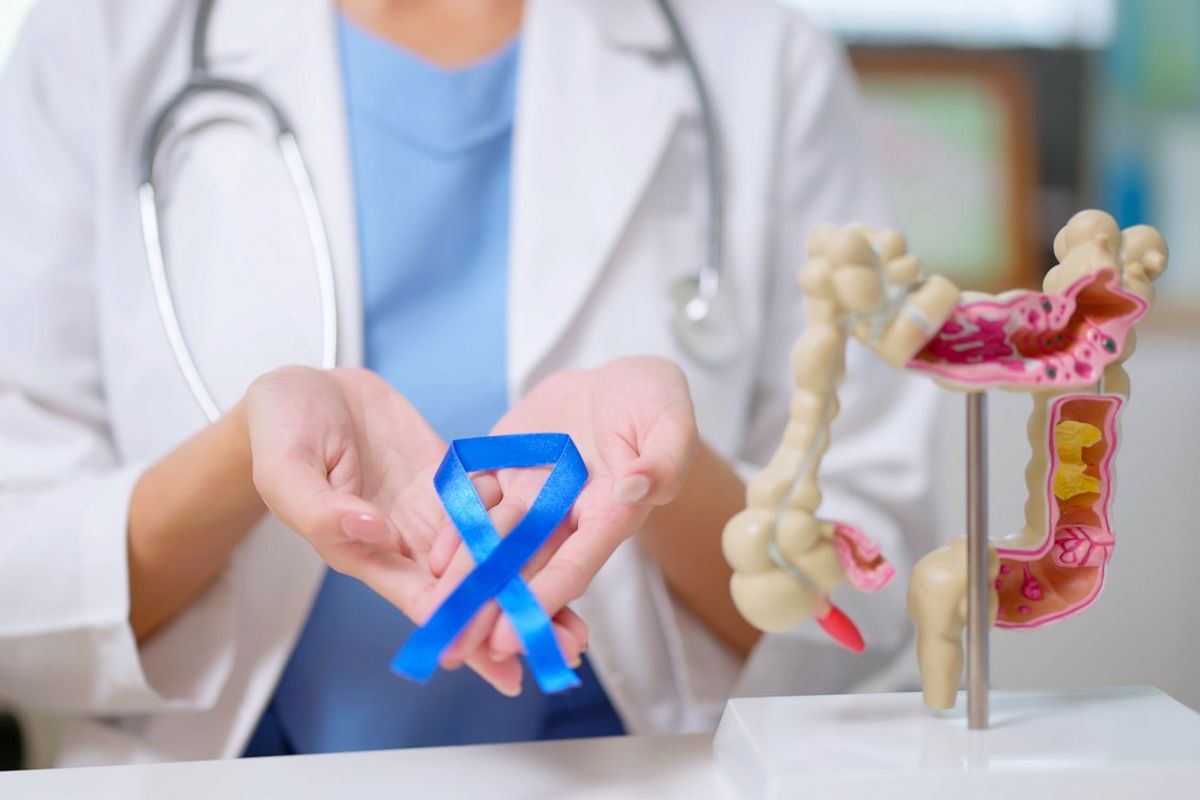close up of female doctor hand wear white coat holds blue ribbon in front of her chest with colon model on table