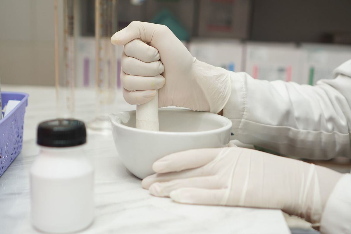 close up of pharmacists mixture a medicine with a mortar and using glove