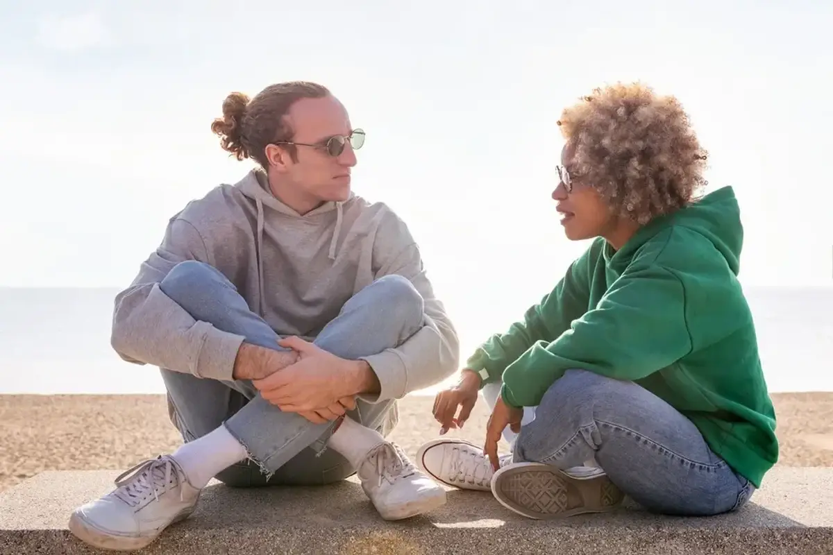 couple chatting at sunset seated on a bench by the beach