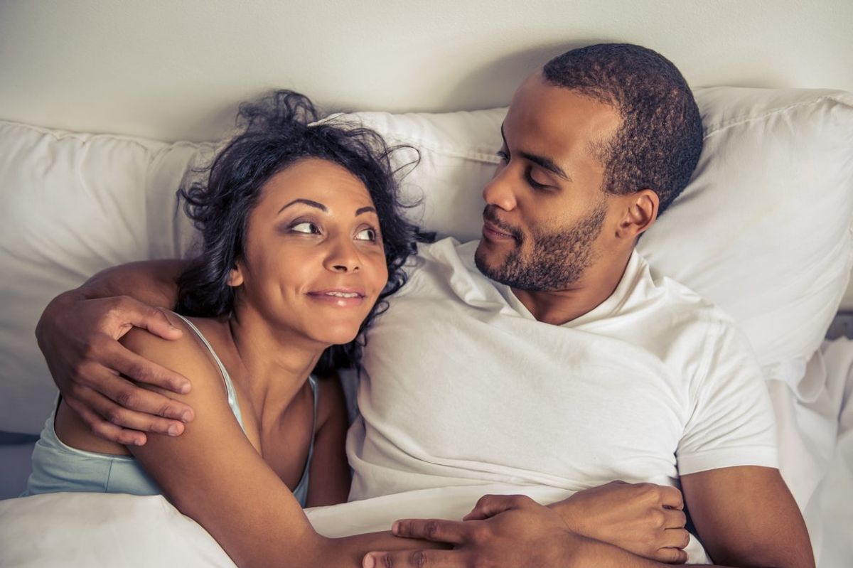 couple hugging, looking at each other and smiling while lying in bed at home