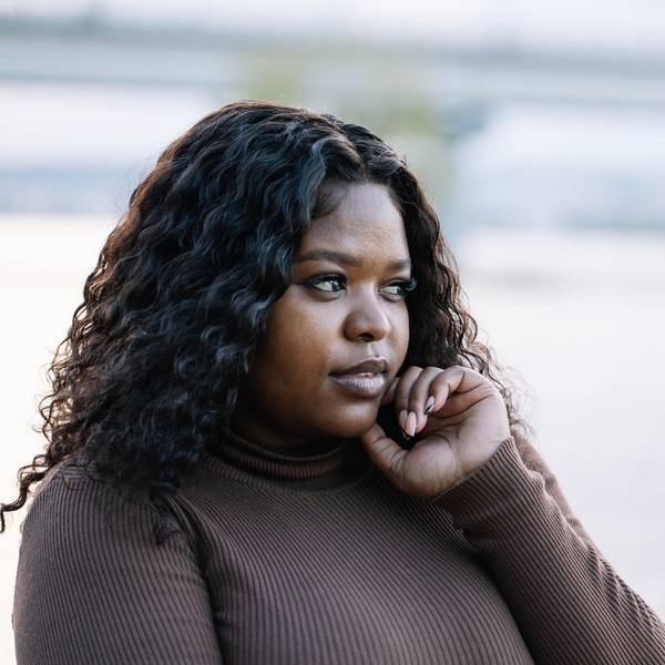 Curly black-haired cute serious plump African Afro-American, interracial woman against lake or river on summer vacation