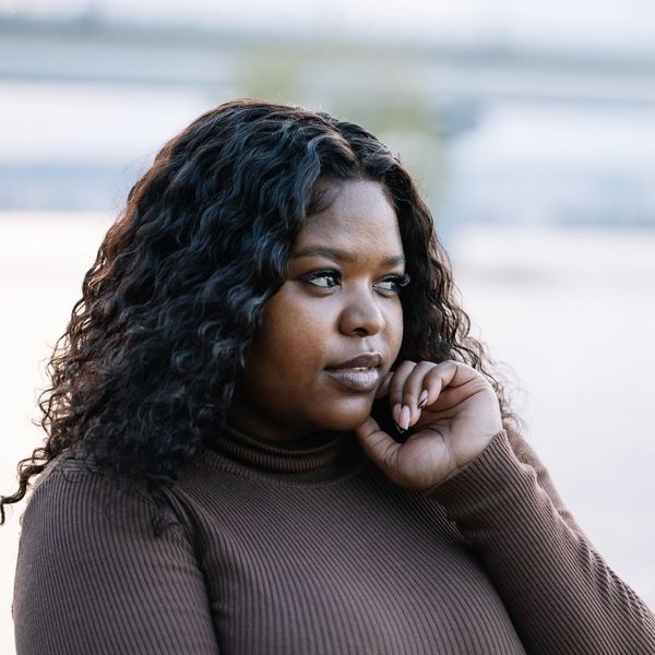 Curly black-haired cute serious plump African Afro-American, interracial woman against lake or river on summer vacation