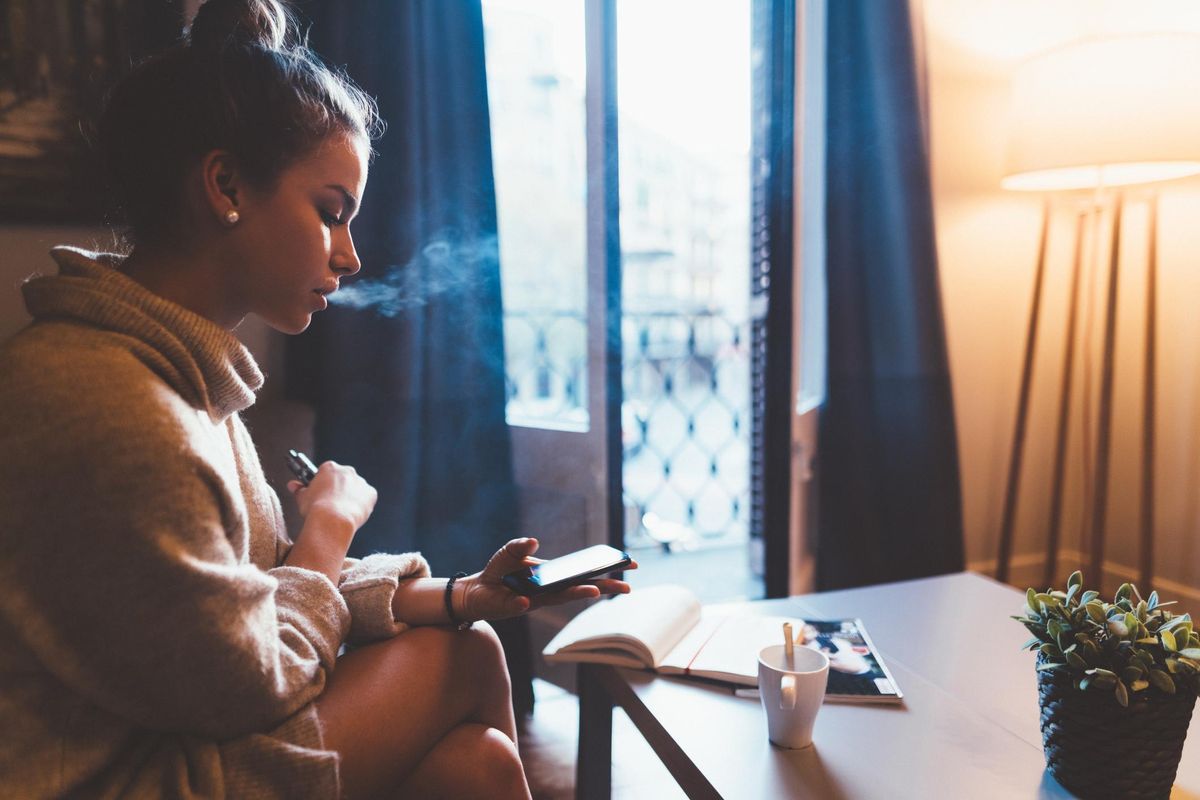 Cute girl in Barcelona smoking e-cigarette and using smartphone