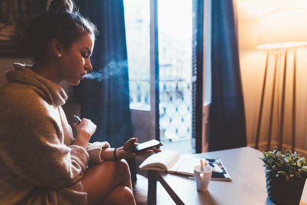 Cute girl in Barcelona smoking e-cigarette and using smartphone