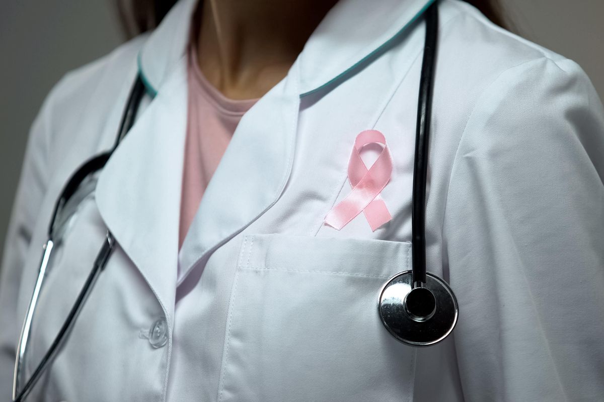 doctor attaching pink ribbon to white medical suit
