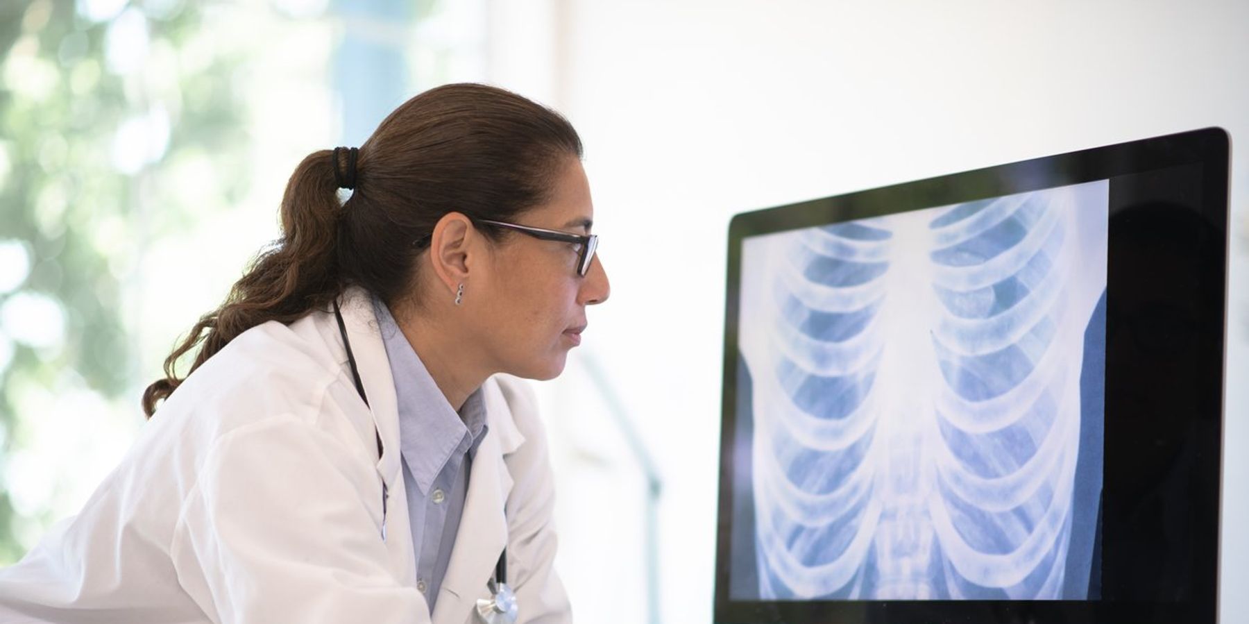 doctor of latino ethnicity leans on her desk and looks at a radiogram of a chest on her desktop computer.