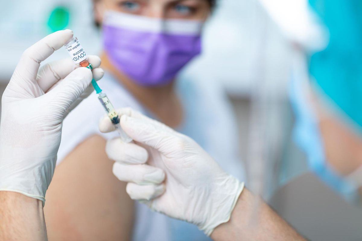 Doctor's hands in surgical gloves preparing COVID-19 vaccine for female patient