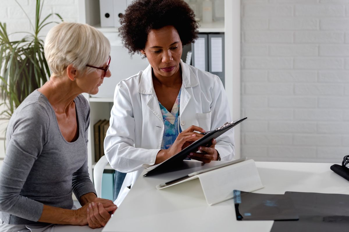 doctor sits at her desk and chats to an elderly female patient about multiple sclerosis