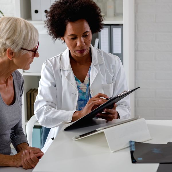 doctor sits at her desk and chats to an elderly female patient about multiple sclerosis