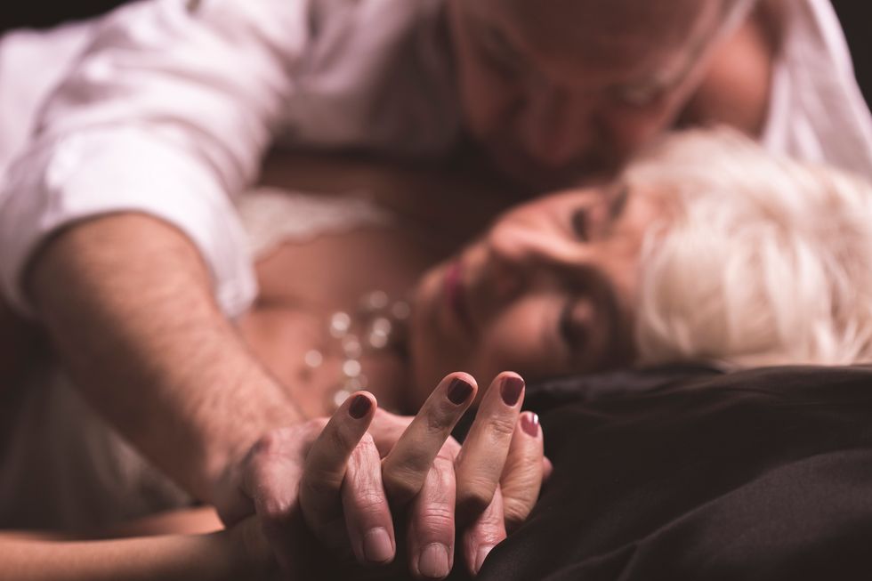 Elder couple lying together on a bed in an erotic love hug with intertwined fingers