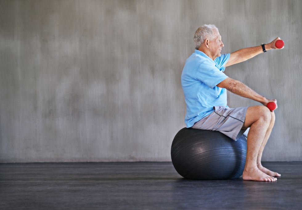 elderly man using weights while sitting on a swiss ball
