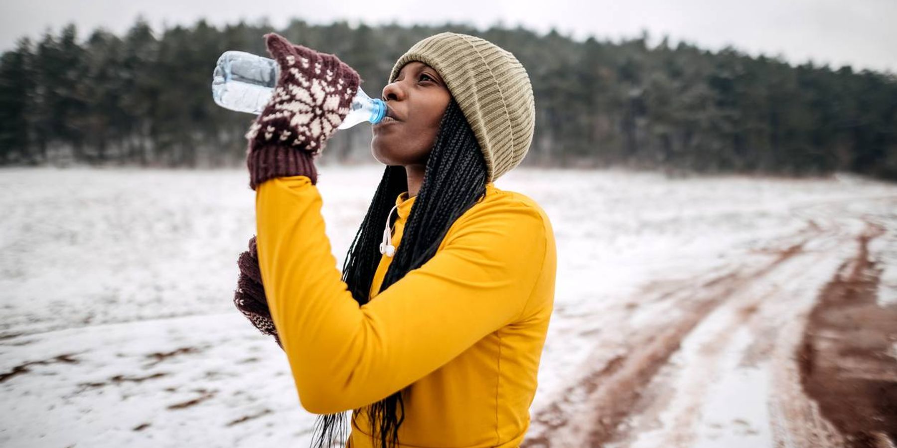 Female athlete in winter clothes drinking water before training on snow