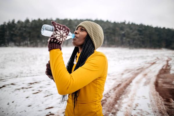 Female athlete in winter clothes drinking water before training on snow