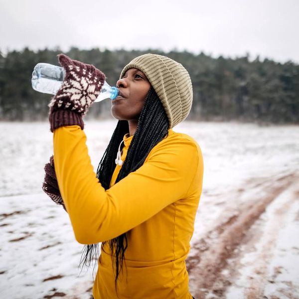 Female athlete in winter clothes drinking water before training on snow
