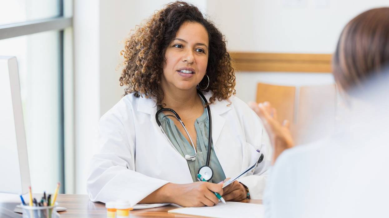 female doctor sits at desk while listening to patient