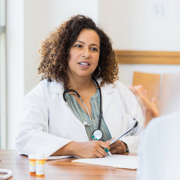 female doctor sits at desk while listening to patient