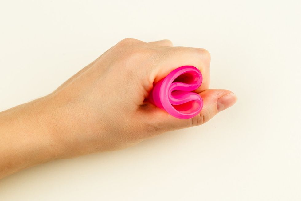 Female hand holding a pink Menstrual Cup folded with a C-Fold Method