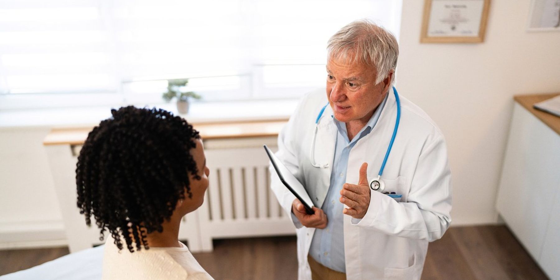 female patient of African-American ethnicity, having an annual medical check-up with a senior male Caucasian doctor