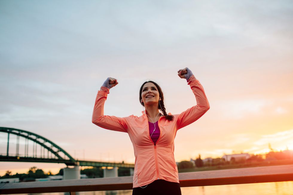 Female Runner Jogging in the city and finishing her training with her hands up in the air screaming with happiness