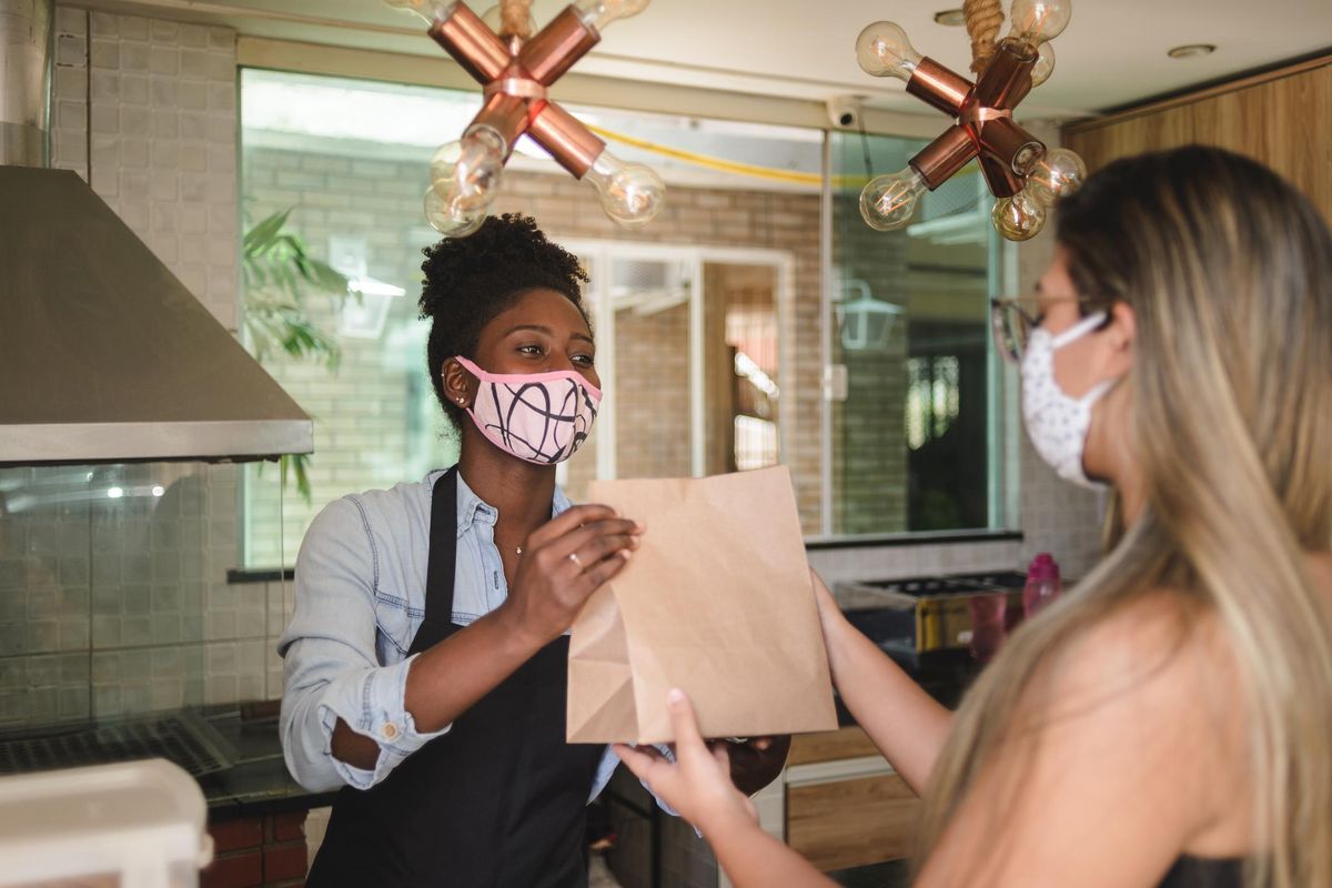 female sales clerk with face mask handing a paper bag to customer