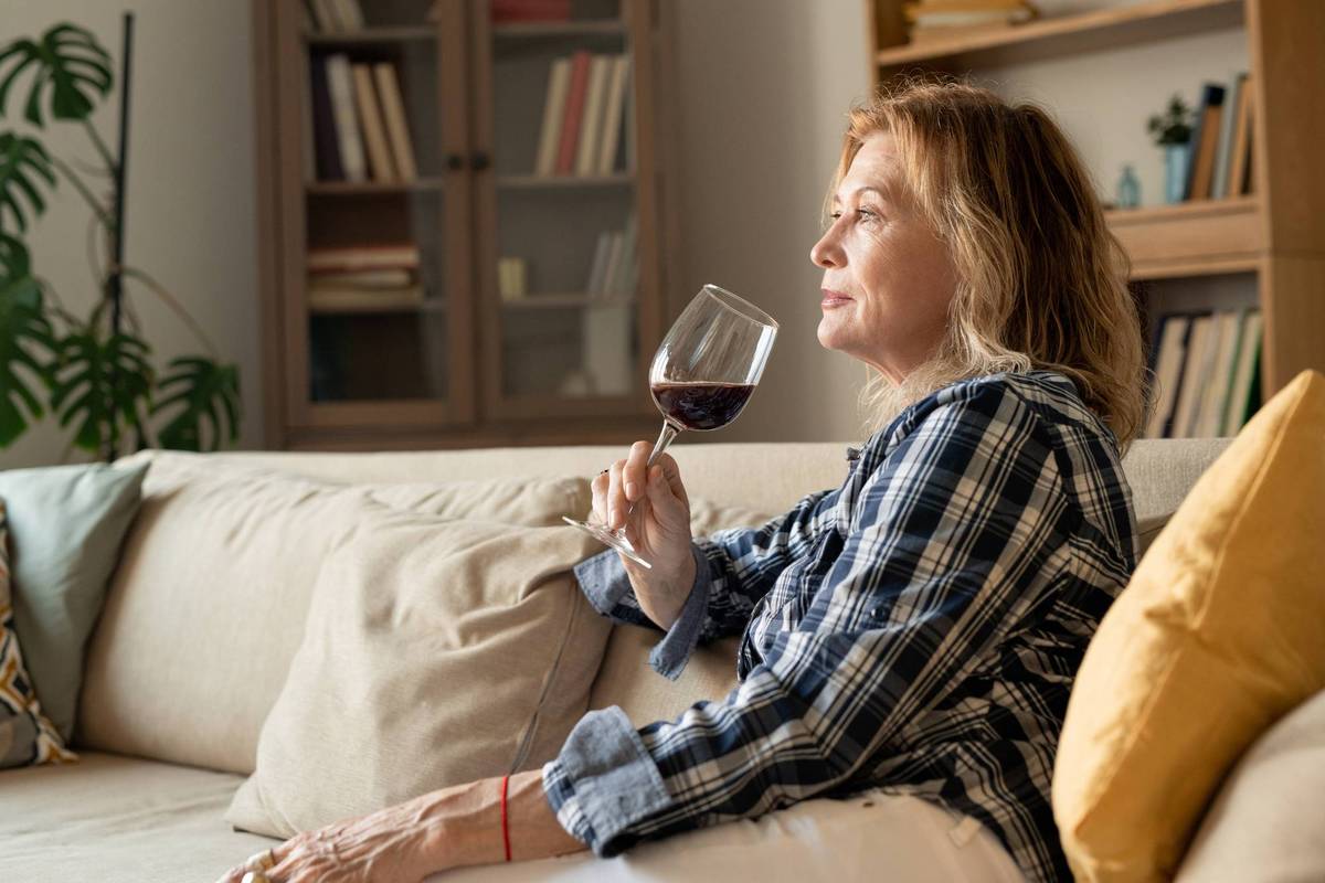 female with glass of red wine leaning against soft pillow while sitting on couch