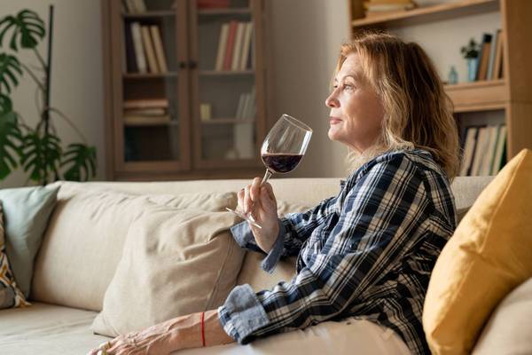 female with glass of red wine leaning against soft pillow while sitting on couch